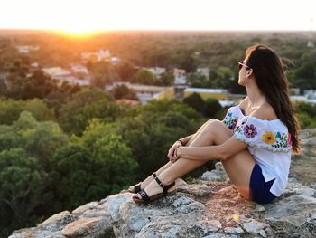 Young woman sitting on landscape against sunset