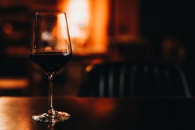 A glass of dark red wine on a wooden table in the evening bokeh light