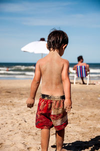 Rear view of shirtless boy walking at beach