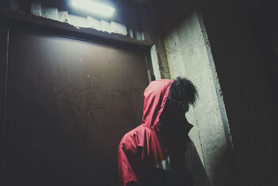 Man wearing hood while standing against wall at night