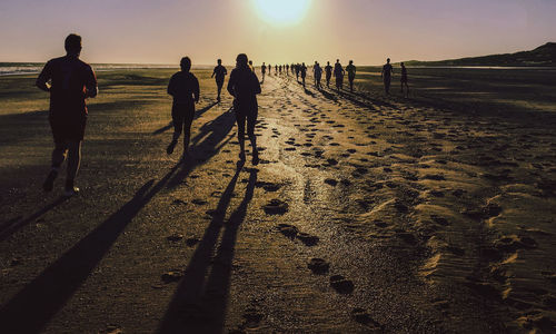 People walking on beach against sky during sunset