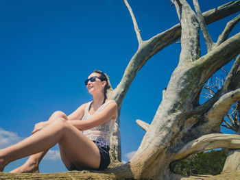 Low angle view of young woman against tree trunk against clear blue sky