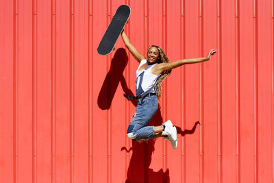 Rear view of woman with arms raised standing against yellow wall