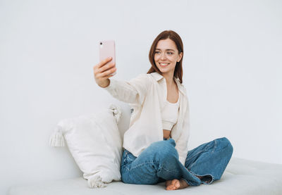 Beautiful smiling woman teenager girl student in white shirt taking selfie on mobile phone in hand