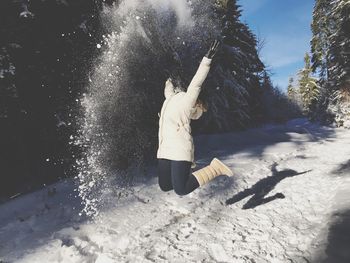 Playful woman jumping over snow covered field in forest