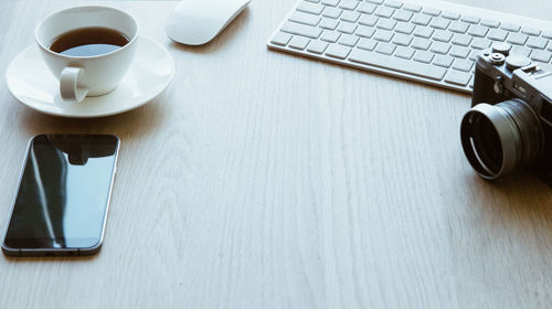 High angle view of coffee cup by keyboard and camera on table