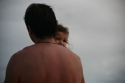 Rear view of shirtless man carrying his daughter