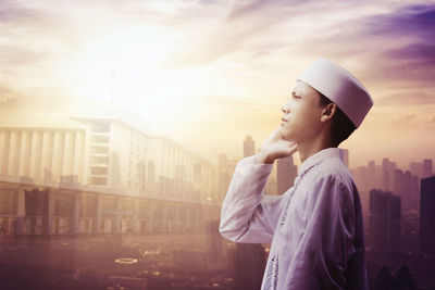 Side view of young woman looking away in city against sky