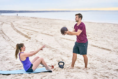 Friends exercising with medicine ball on sand at beach