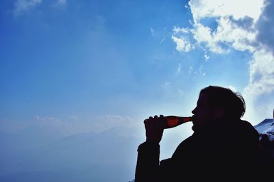 Silhouette man drinking beer against sky