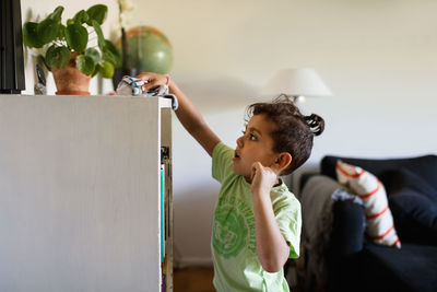 Side view of boy cleaning cabinet with napkin at home