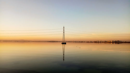 Silhouette cranes by lake against sky during sunset