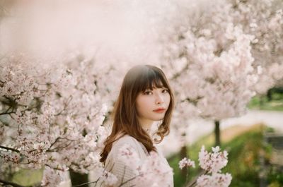 Portrait of woman standing by cherry blossom tree