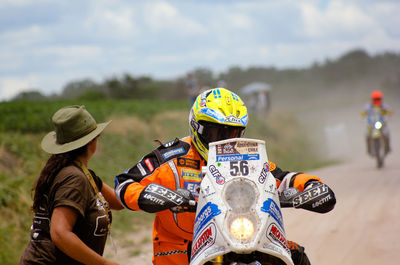 Rear view of man and woman standing on motorcycle against sky