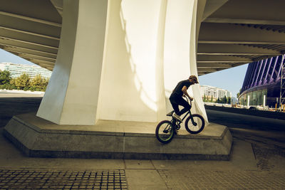 Man riding bicycle on bridge against buildings in city