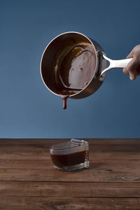 Pouring salted caramel into a glass container on wooden table with blue background