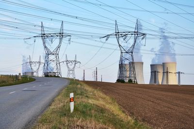 Electricity pylon on field by road against sky