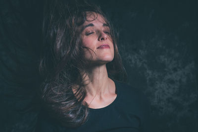 Young woman with closed eyes and tousled hair against wall