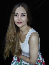 Portrait of young woman standing against black background