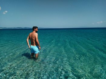 Full length of shirtless man standing in sea against sky