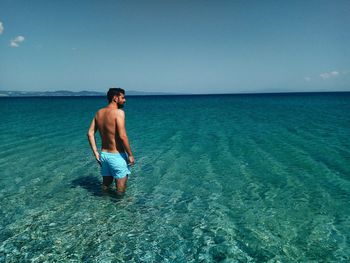 Rear view of shirtless man standing in sea against sky