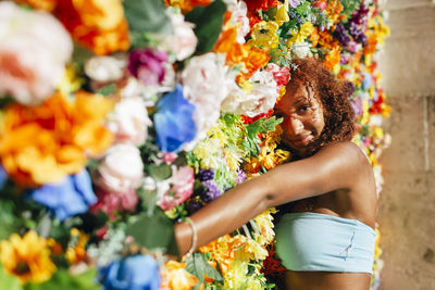 Smiling young woman leaning on multi colored flower wall