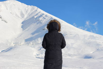 Rear view of man standing on snowcapped mountain against sky