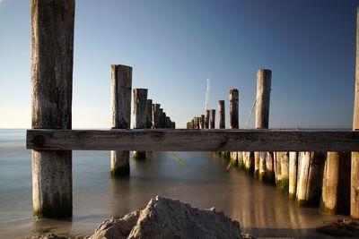 Wooden posts in sea against clear sky