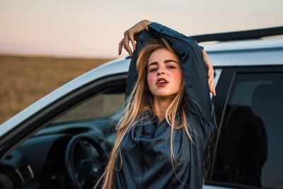 Portrait of young woman standing by car