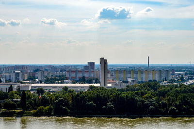 Scenic view of river in front of cityscape against cloudy sky