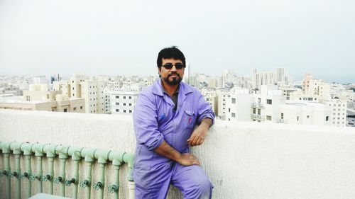 Portrait of young man standing against buildings in city