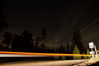 Light trails on trees against sky at night