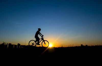 Silhouette boy riding bicycle on field during sunset