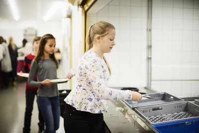 Girl putting plate in crate after having lunch at school cafeteria