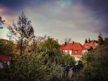 House and trees by plants against sky