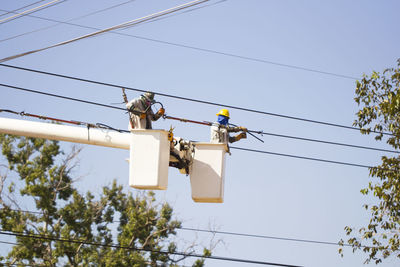 Low angle view of workers in cherry pickers repairing power line