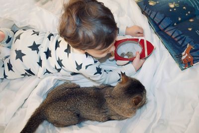 Directly above shot of boy holding piggy bank by cat on bed