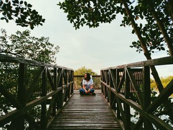 Young woman sitting cross legged on footbridge