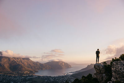 Rear view of male hiker standing on cliff against sky during sunset