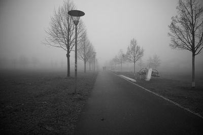 Road by bare trees on field against sky