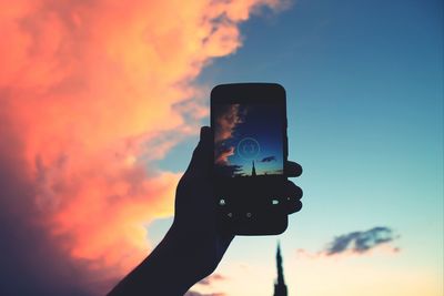 Cropped image of silhouette person holding cell phone against sky at dusk