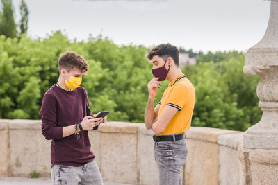 Young man using mobile phone while standing with friend