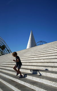 Full length of girl moving down on steps against clear blue sky