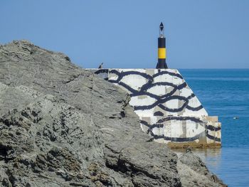 Lighthouse by sea against clear blue sky