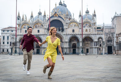 Smiling couple running against historic building