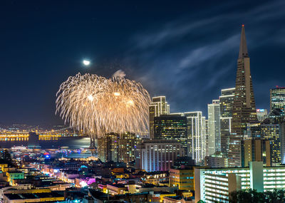 Firework display over illuminated buildings against sky at night