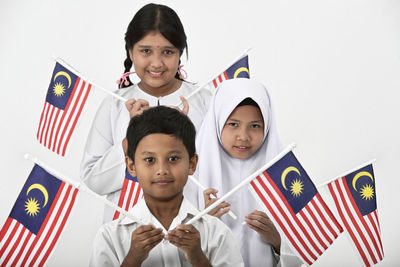 Portrait of students holding malaysian flag standing against white background