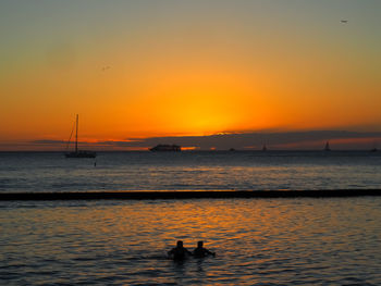 A couple swimming gaze at the setting sun off waikiki beach hawaii