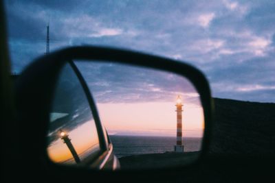 Reflection of light house seen on side-view mirror of car during sunset