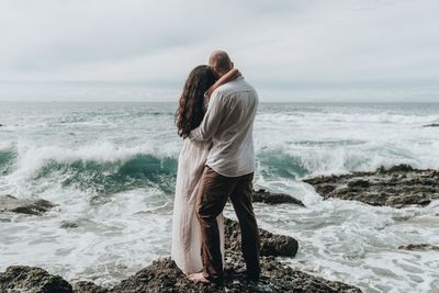 Couple embracing at beach against sky